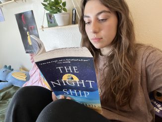 A young woman reads a book. Behind her is a wall decorated with hanging shelves, which hold potted plants and picture frames, and movie posters.