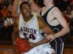 Basketball players in intense game action; one in white jersey with "Albion" attempts a shot while being defended by a player in black. Crowd watches intently.