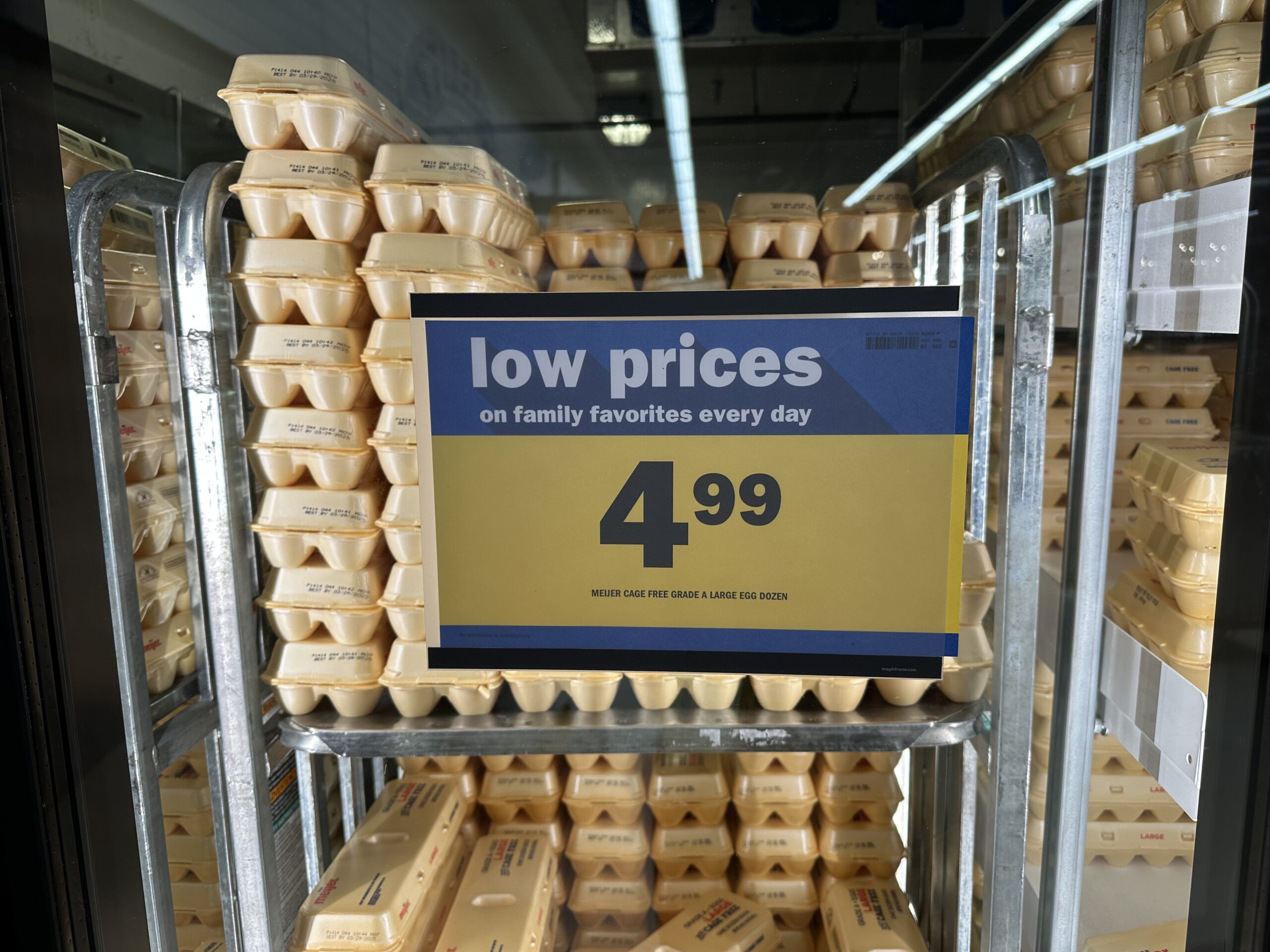 A big yellow sign with the price $4.99 displayed on it stuck on the glass in front of stacks of egg cartons. 