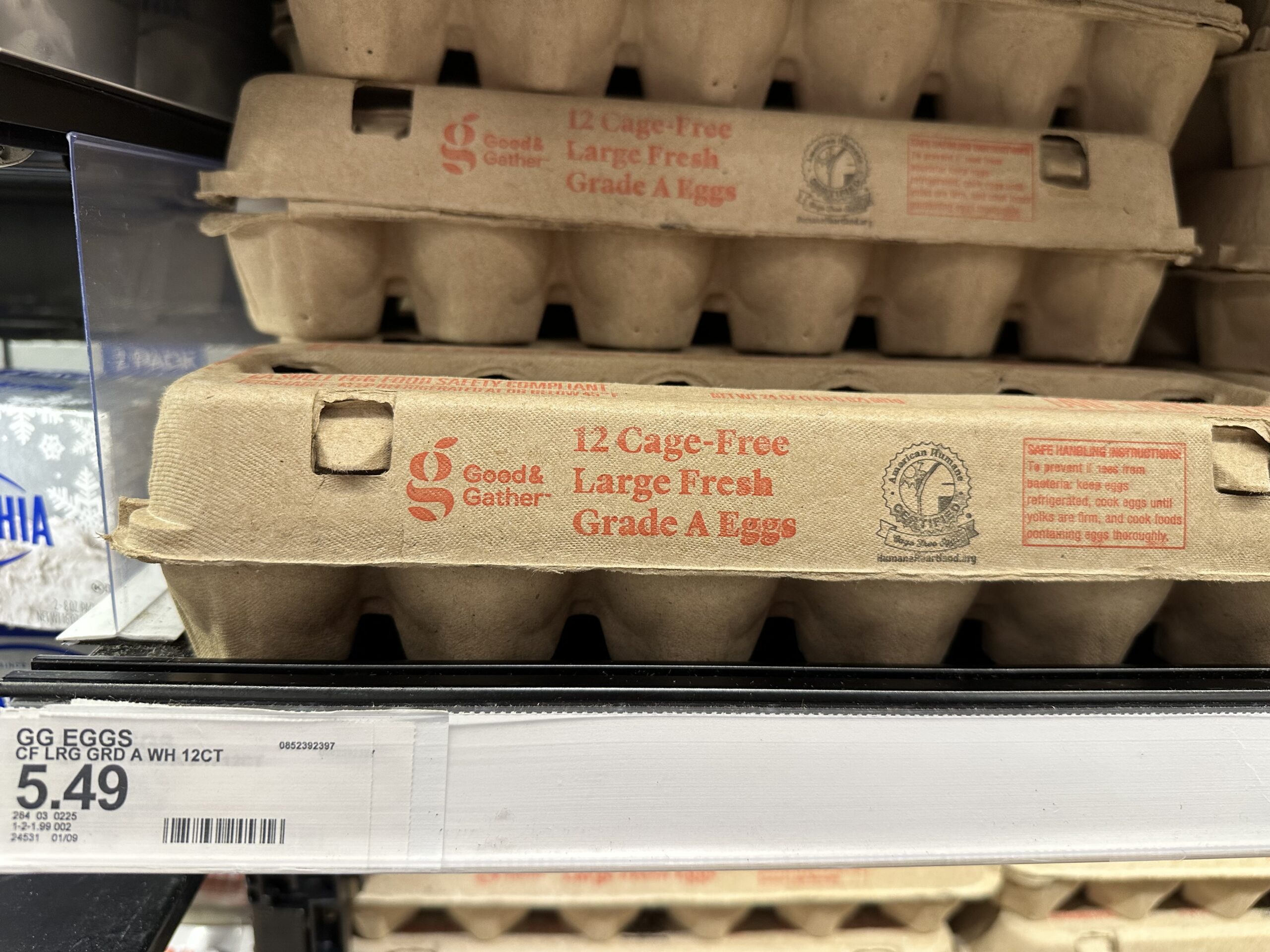 Several brown cartons of eggs stacked on top of each other, with a white price tag sticker in the bottom left corner that reads $5.49. 