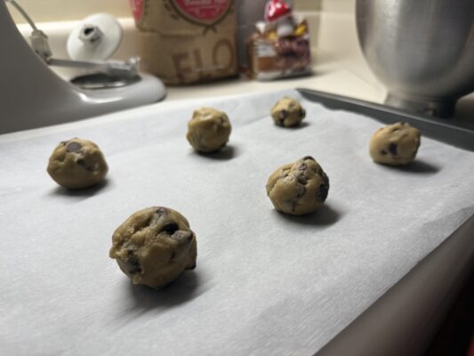 Medium sized cookie dough balls evenly spaced on a sheet of parchment paper and cookie sheet.