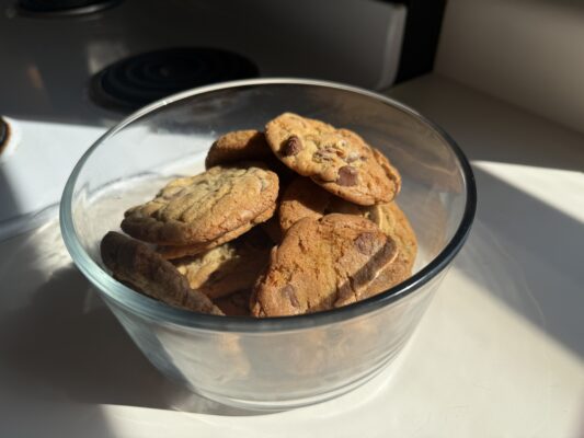 A glass container filled with freshly baked chocolate chip cookies.