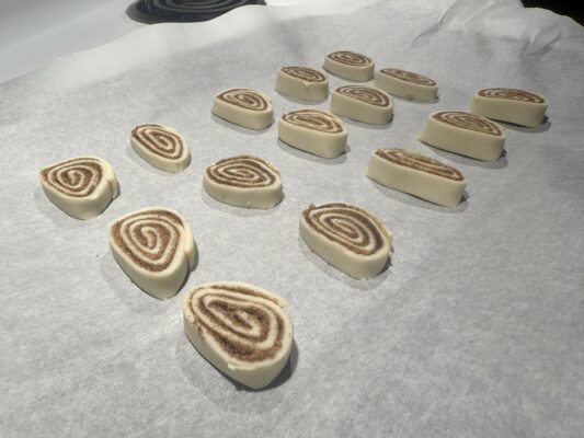 15 unbaked golden brown pie crust cinnamon rolls with melted sugar and cinnamon sit evenly-spaced on a sheet of parchment paper.
