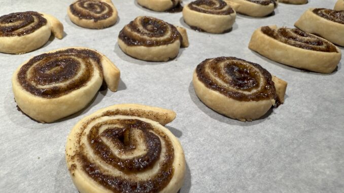15 golden brown pie crust cinnamon rolls with melted sugar and cinnamon inside them sit evenly spaced on a sheet of parchment paper.