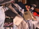 A young woman with dark hair lays in a bed with light blue striped covers and a pillow under her head. Her eyes are closed, and she holds the covers up over her face. On the surrounding bed are four books, one in focus with the cover visible reading “The Neuroscience of Sleep and Dreams.”