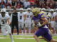 A football player in a purple Albion uniform runs with the ball, pursued by Alma opponents in white. The crowd watches, creating a tense, action-packed scene.