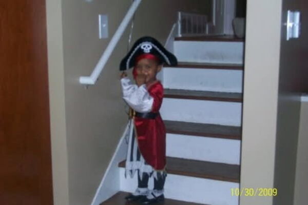 A two-year-old child standing on steps, dressed in a red pirate costume.