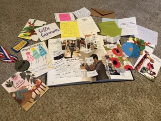 Colorful cards surround an open yearbook, sprinkled with handwritten notes on a beige carpet. Along the outskirts of the cards is a medal.