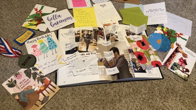 Colorful cards surround an open yearbook, sprinkled with handwritten notes on a beige carpet. Along the outskirts of the cards is a medal.