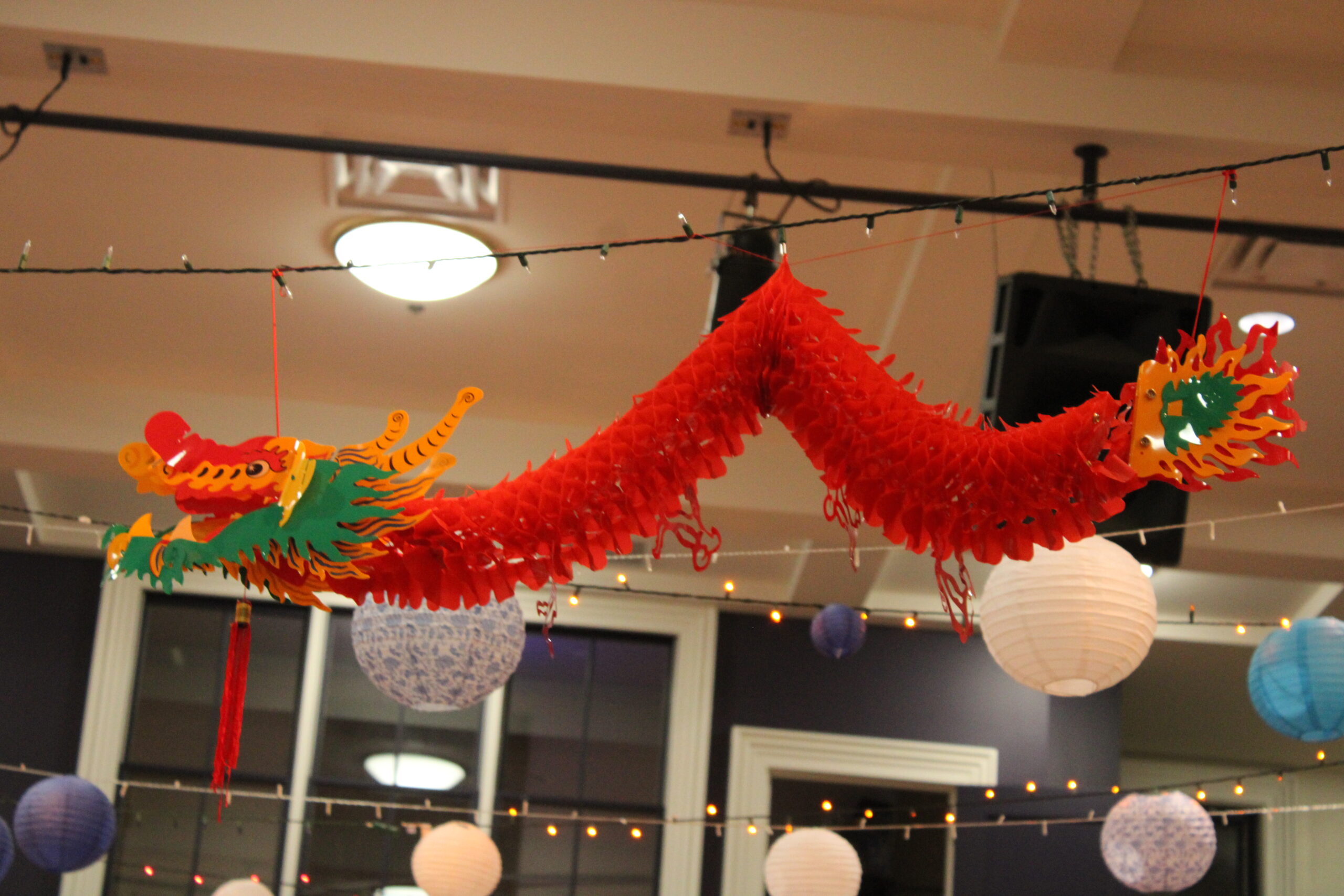 A red, snake-like paper dragon decoration is strung up by red strings. It is attached to a string of lights by the ends and middle.