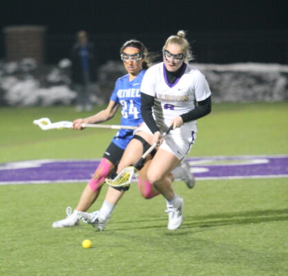 Two lacrosse players fight for possession of the ball in the midst of a field.