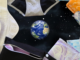 A 3D Earth sits in the middle of the image against a background of black space, dotted with white stars. In the foreground, framing the image, are several period products, including disposable and cloth pads, tampons, and a pair of period underwear.