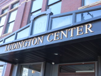 A photograph of the outside of the Ludington Center in downtown Albion. There is a large black sign centered in the photograph with gold letters spelling out ‘Ludington Center,’ along with the building number 101 above it in transparent text.
